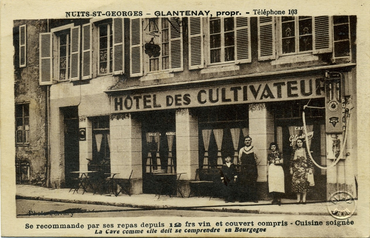 Figure 7: Postcard depicting the shop front for l’hôtel des Cultivateurs in Nuits-Saint-Georges (years 1931-1934). At right, a wall-mounted petrol pump. Source: Musée de la Vie bourguignonne Perrin de Puycousin.